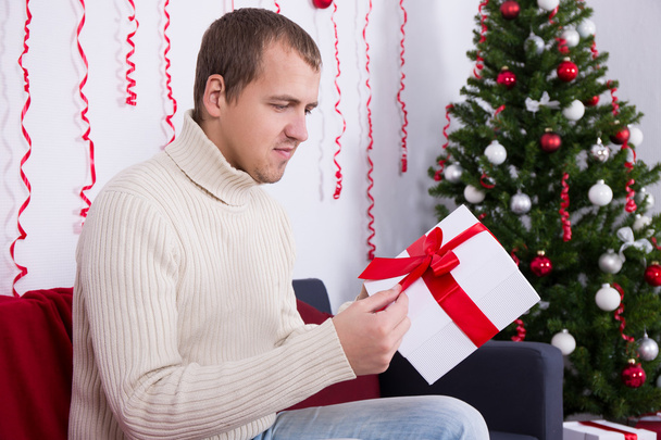 christmas concept - happy young handsome man opening gift in liv - Фото, изображение