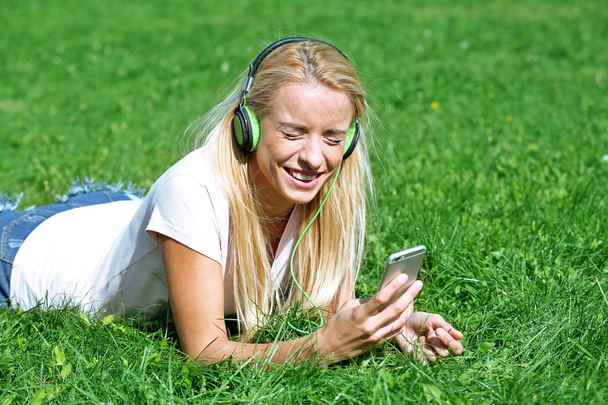 Young woman with earphones and smartphone listening to music on grass - Foto, immagini