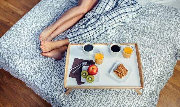 Terveellinen aamiainen tarjottimella ja pari jalat sängyn yli
 - Valokuva, kuva