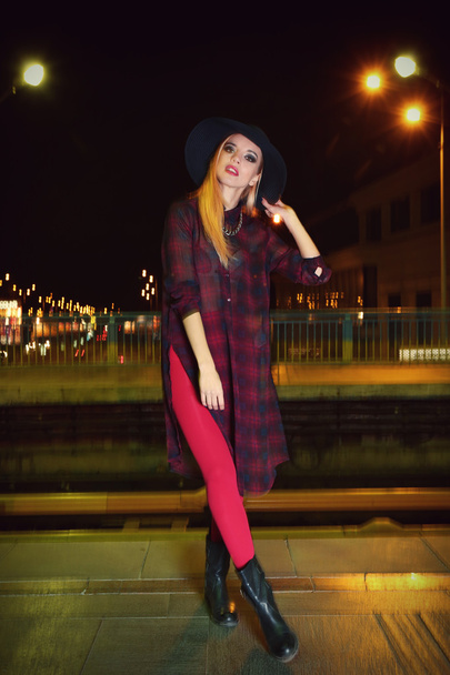 Happy stylish woman in hat  poses on the bridge at night - Фото, изображение
