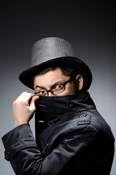 Mladý muž v černém kabátě a klobouku proti šedi - Fotografie, Obrázek