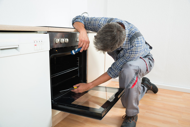 Repairman Examining Oven With Flashlight - Фото, изображение