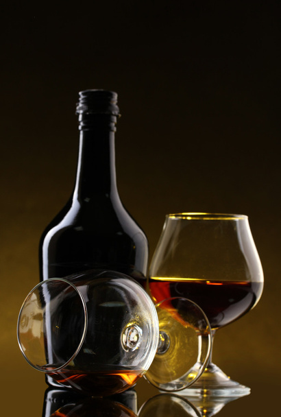 Glasses of brandy and bottle on yellow background - Foto, Bild
