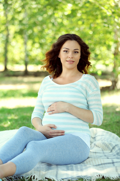 Cute happy pregnant woman on white blanket in the park - Фото, изображение