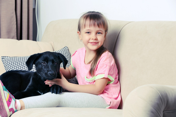 Little girl with puppy on sofa - Fotó, kép