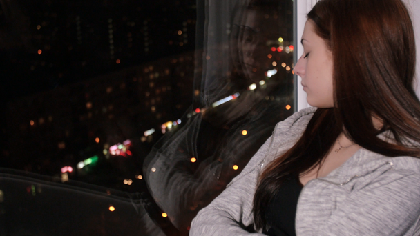 Mujer triste se sienta en el alféizar de la ventana, mira la ciudad de la noche
 - Imágenes, Vídeo