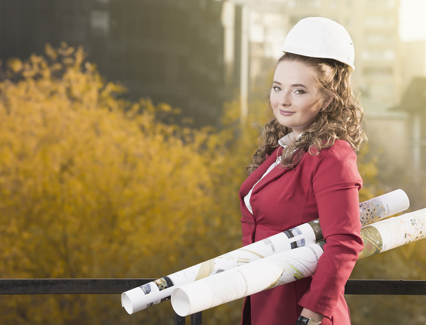 Smiling businesswoman in helmet studying the sketch of future business centre. Attractive lady in business suit is satisfied by the plan made by architect. - Photo, Image
