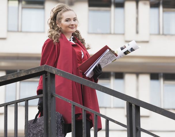young beautiful woman architect in red jacket standing near the railing with the drawings lestnitsy.Student - Photo, Image