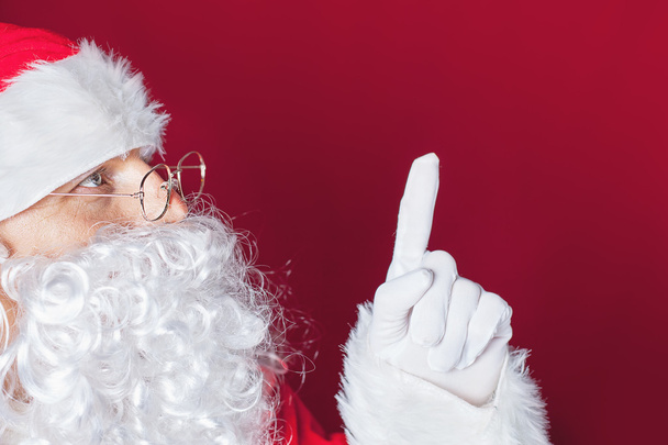 Santa Claus pointing at copy space, red background - Fotografie, Obrázek