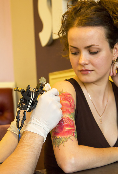 tattooer showing process of making a tattoo on young beautiful hipster woman with red curly hair hand. Tattoo design in the form of rose - Fotó, kép