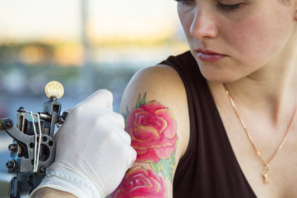 tattooer showing process of making a tattoo on young beautiful hipster woman with red curly hair hand. Tattoo design in the form of rose - Photo, Image