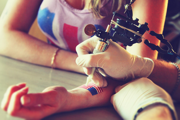 tattooer showing process of making a tattoo on young beautiful hipster woman with blonde hair hand. Tattoo design in the form pin-up girl with flower head - Φωτογραφία, εικόνα