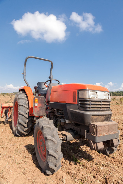 Tractor rojo pequeño con arado en el campo. Cielo nublado
 - Foto, imagen