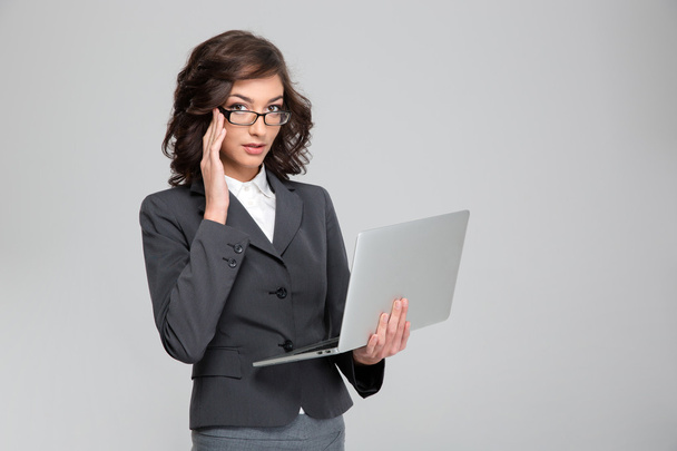 Young businesswoman holding laptop and touching her glasses - Foto, imagen