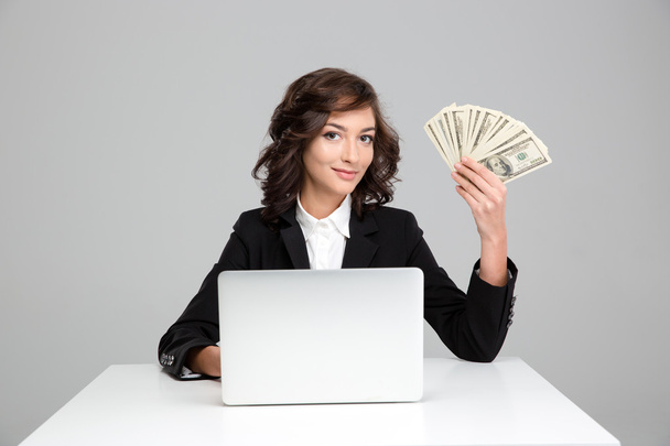 Pretty young woman using laptop and showing money - Foto, afbeelding
