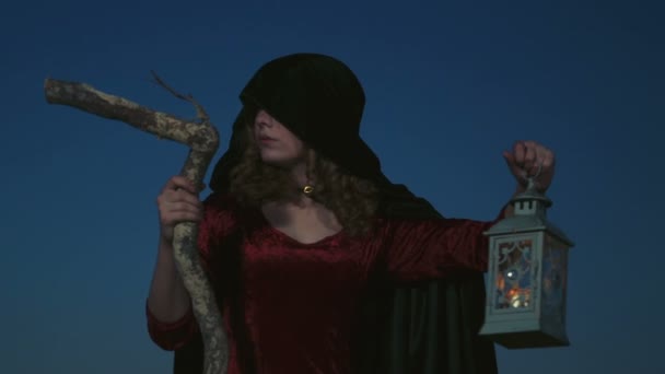 mladá žena, oblečená jako čarodějnice pózuje s holí a lampa - Záběry, video