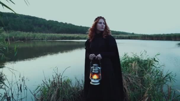 młoda kobieta sobie staromodny sukienka i płaszcz stojący w pobliżu jeziora - Materiał filmowy, wideo