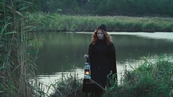 female dressed in old-fashioned clothes holding a lamp standing near the lake - Footage, Video