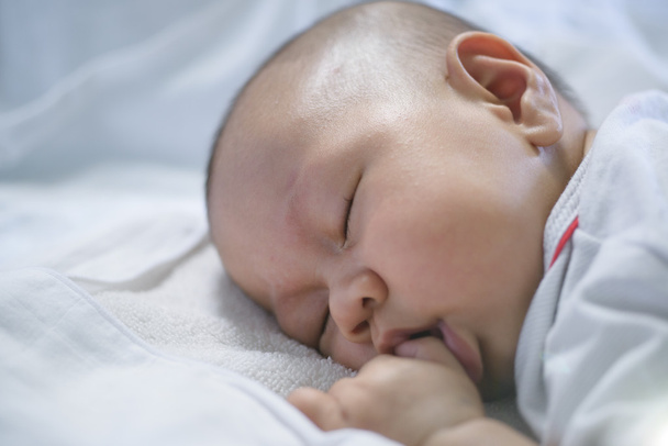 白いベッドリネンを眠っているアジアの赤ちゃん. - 写真・画像