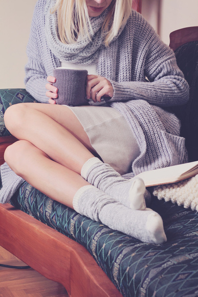 Beautiful Woman wearing  cozy sweater and Warm Wool Socks  reading a book sitting on comfortable sofa enjoying hot chocolate drink . Winter, Christmas  holidays concept. - Fotoğraf, Görsel