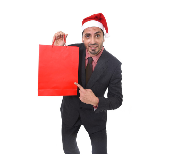 joven atractivo hombre de negocios en Navidad Santa sombrero celebración y señalando bolsa de compras roja en diciembre y la venta de año nuevo
 - Foto, Imagen