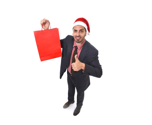 young attractive businessman in Christmas Santa hat holding red shopping bag in December and New year sale - Zdjęcie, obraz