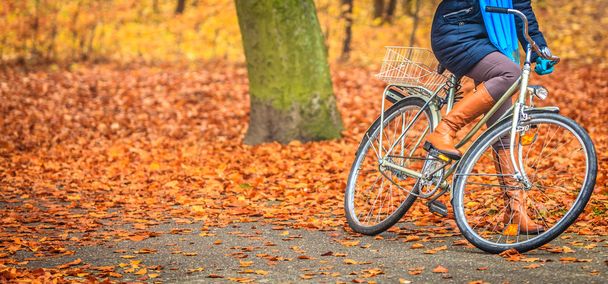 Active woman riding bike in autumn park. - Foto, afbeelding