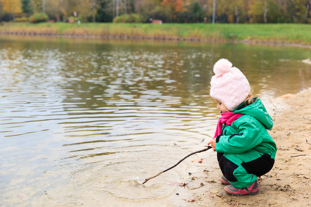 little girl playing with water and stick in autumn - Photo, Image