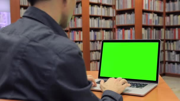 junger hübscher Mann sitzt und arbeitet auf grünem Bildschirm - Filmmaterial, Video