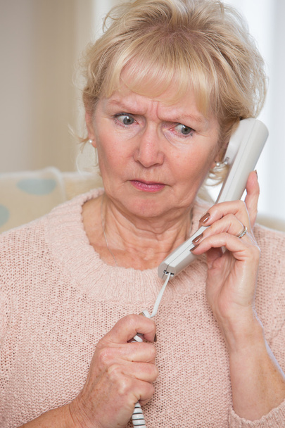 Huolestunut vanhempi nainen, joka vastaa puhelimeen kotona
 - Valokuva, kuva