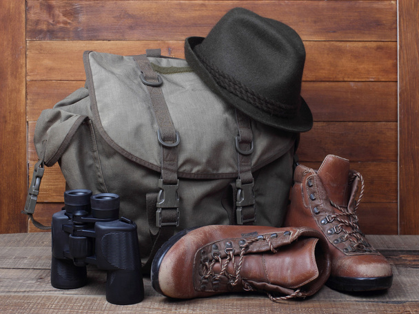 Rucksack com botas velhas, binocular e chapéu sobre fundo de madeira
 - Foto, Imagem