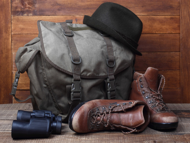 Rucksack mit alten Stiefeln, Fernglas und Hut auf Holzgrund - Foto, Bild