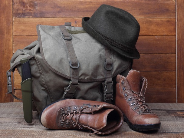 Rucksack with old boots, knife and hat on wooden background - Photo, Image
