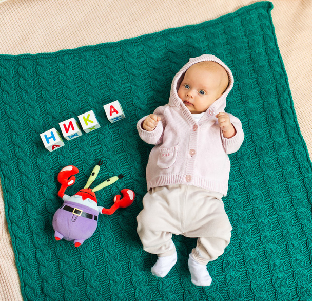 de baby in luiers ligt op een cover onder speelgoed - Foto, afbeelding