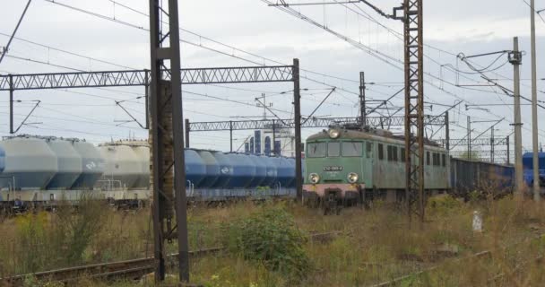 Φορτηγό τρένο στέκεται στην πιο μακριά σιδηροδρομική τροχιά πράσινη ηλεκτρική ατμομηχανή τραβά μεγάλη φορτίου τρένο γκρι και μπλε εμπορευματικές άμαξες συννεφιασμένη ημέρα του φθινοπώρου - Πλάνα, βίντεο