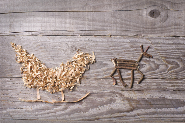 Simple symbols of Father Christmas sleigh arranged from sawdust and reindeer made from dry wooden sticks on wooden grey background. - Photo, Image