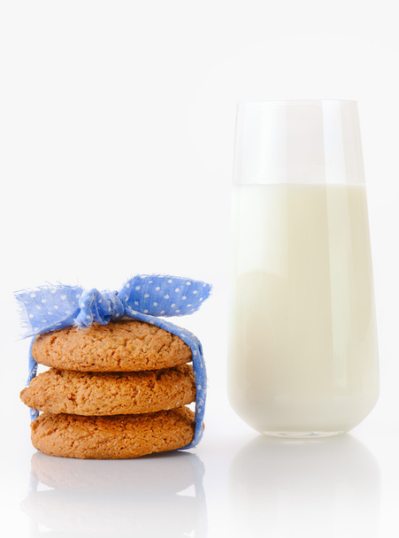 Три домашние овсяные печенья, завязанные голубой лентой в маленькие белые точки в горошек и стакан молока
 - Фото, изображение