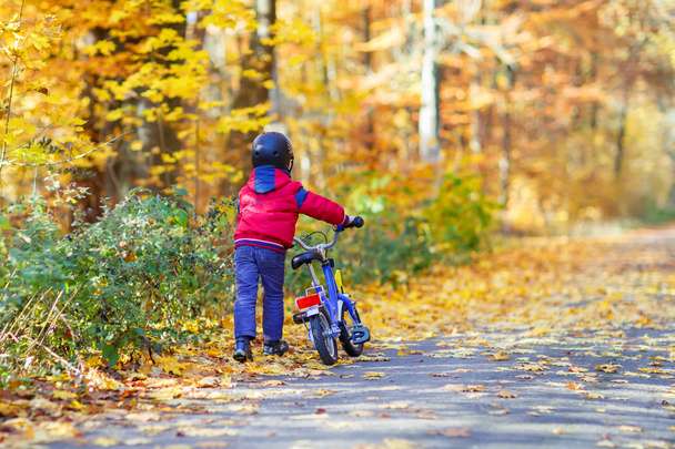 Little kid boy with bicycle in autumn forest - Fotó, kép