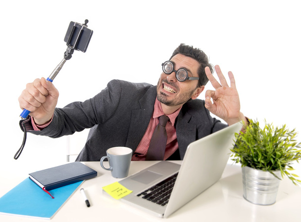funny nerd businessman at office desk taking selfie photo with mobile phone camera and stick - 写真・画像