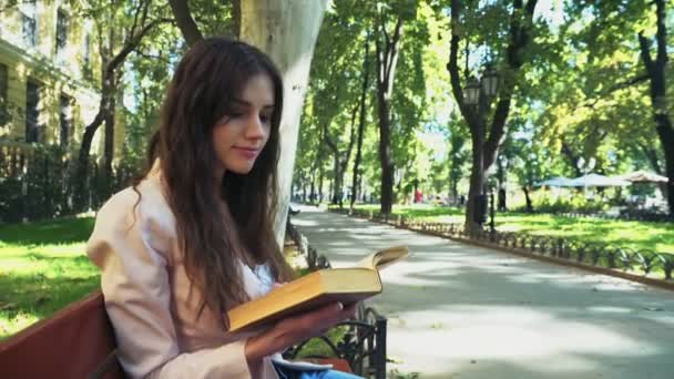 female student reading a book on a bench in park - Video