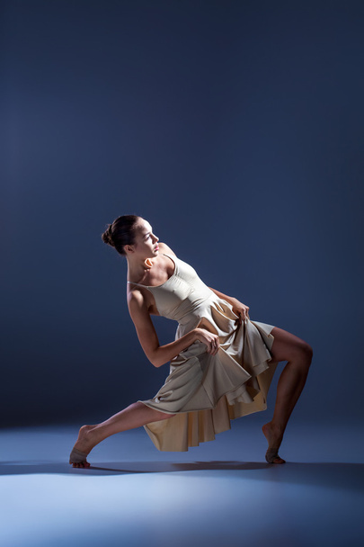 Young beautiful dancer in beige dress dancing on gray background - Fotó, kép
