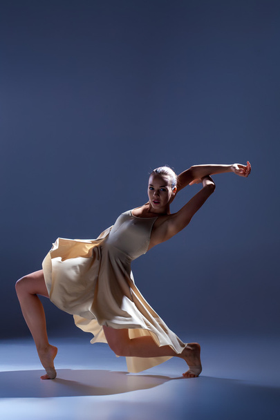 Young beautiful dancer in beige dress dancing on gray background - Foto, afbeelding
