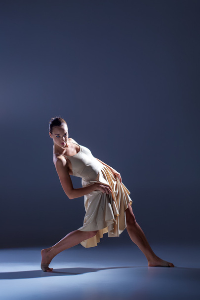 Young beautiful dancer in beige dress dancing on gray background - Foto, imagen