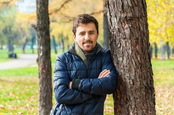 Handsome guy leaned against a tree in autumn park - Fotó, kép