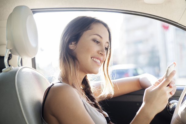 Young woman sending a message with her mobile phone sitting in her car - Photo, image