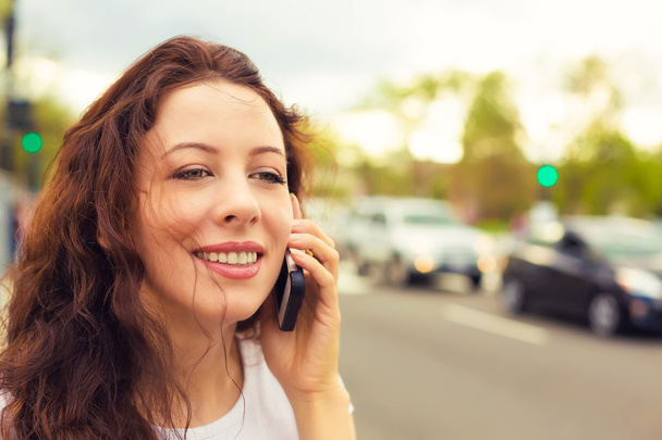Happy young lady talking on mobile phone walking on a street  - Фото, изображение