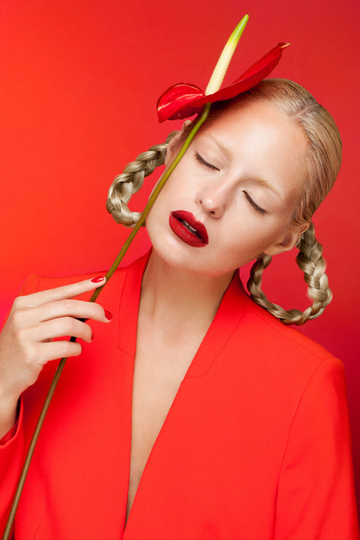 Sensual charming sexy blonde woman in red jacket posing in studio taking red calla on her hand, red background. - Zdjęcie, obraz