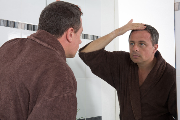 Peilin edessä oleva mies katsoo hiuksiaan.
 - Valokuva, kuva
