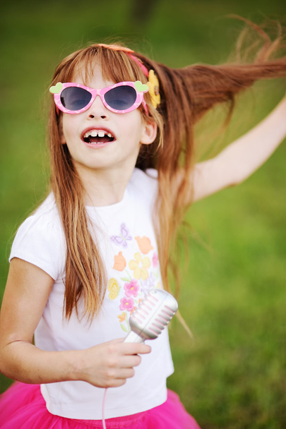 cheerful red-haired girl in sunglasses singing into a microphone - Foto, immagini