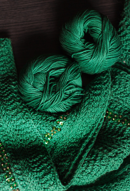 Два шара глубокой зеленой пряжи и зеленый шарф с бисером лежит на да
 - Фото, изображение